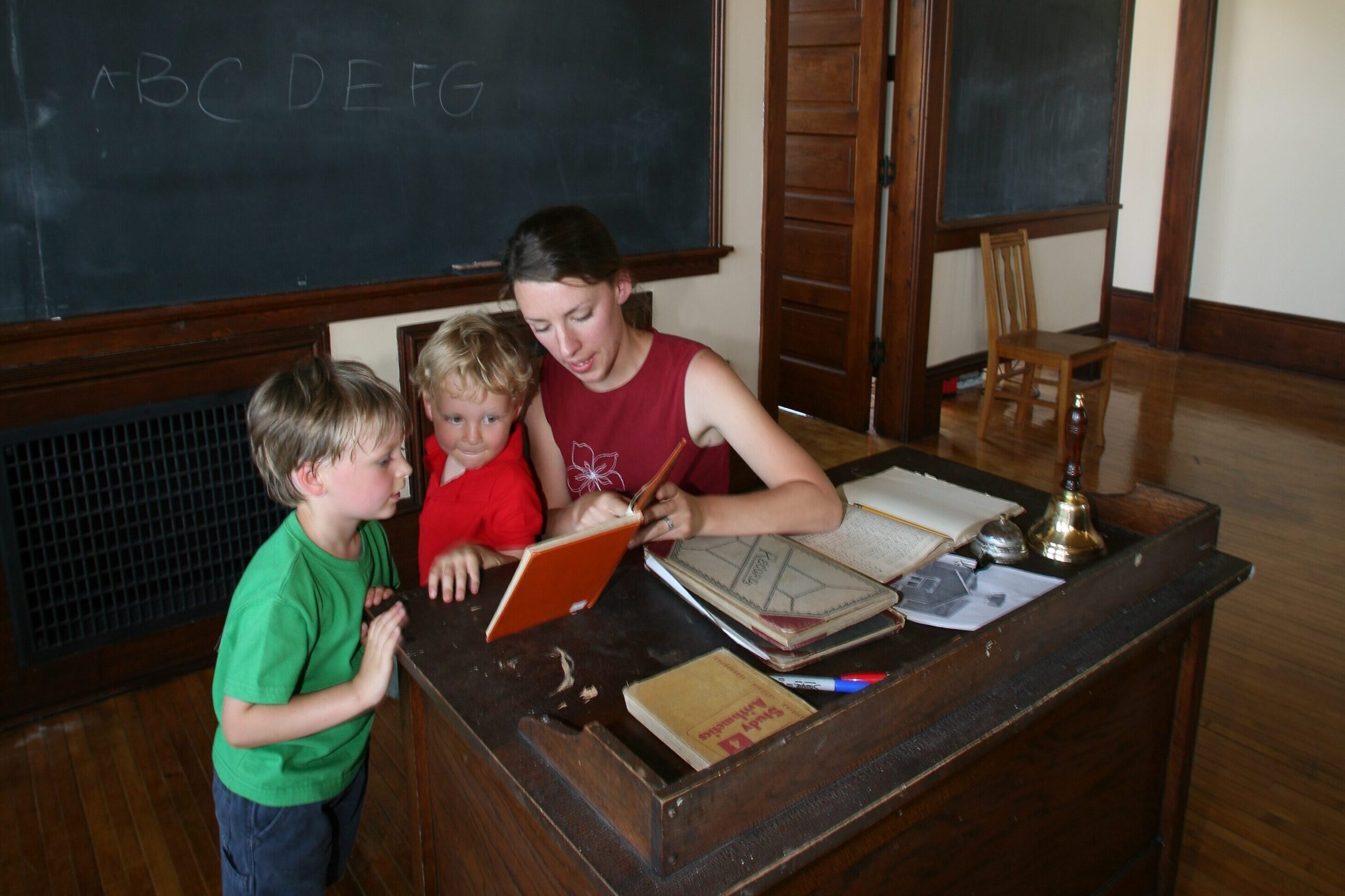 two boys looking at a book while their mother points at something